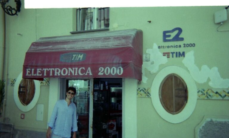 Ingresso di un negozio di elettronica con un’insegna rossa e vetrina esposta.