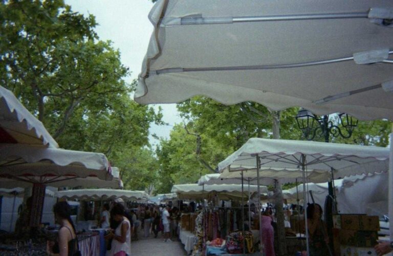 Mercatino all’aperto con bancarelle sotto tende bianche e persone che passeggiano tra gli espositori.