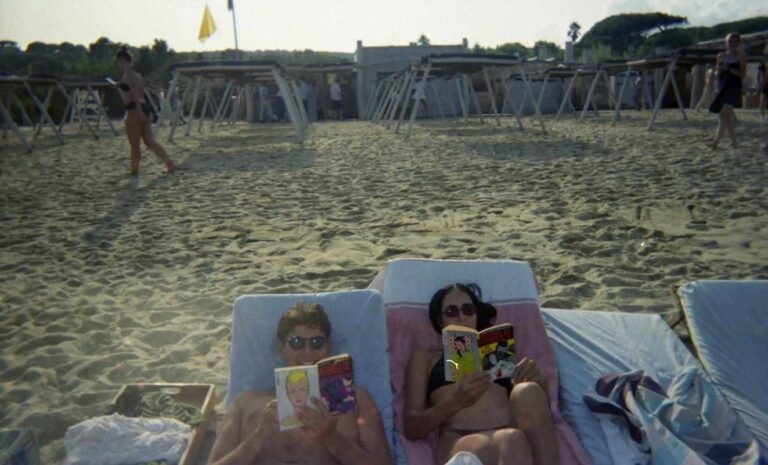 Due persone che leggono fumetti sdraiate sui lettini del Club 55 a Saint-Tropez.