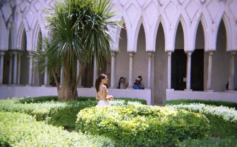 Donna che passeggia nel giardino di un chiostro con colonne e archi medievali.